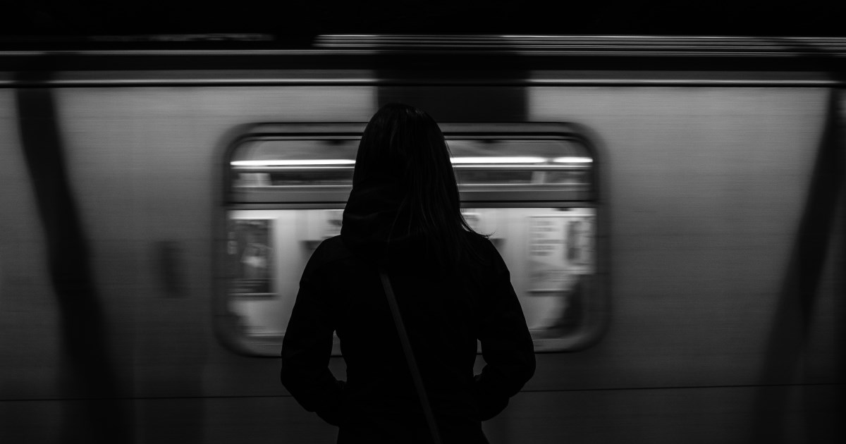 Lone figure standing on a subway platform, with a subway car whizzing past
